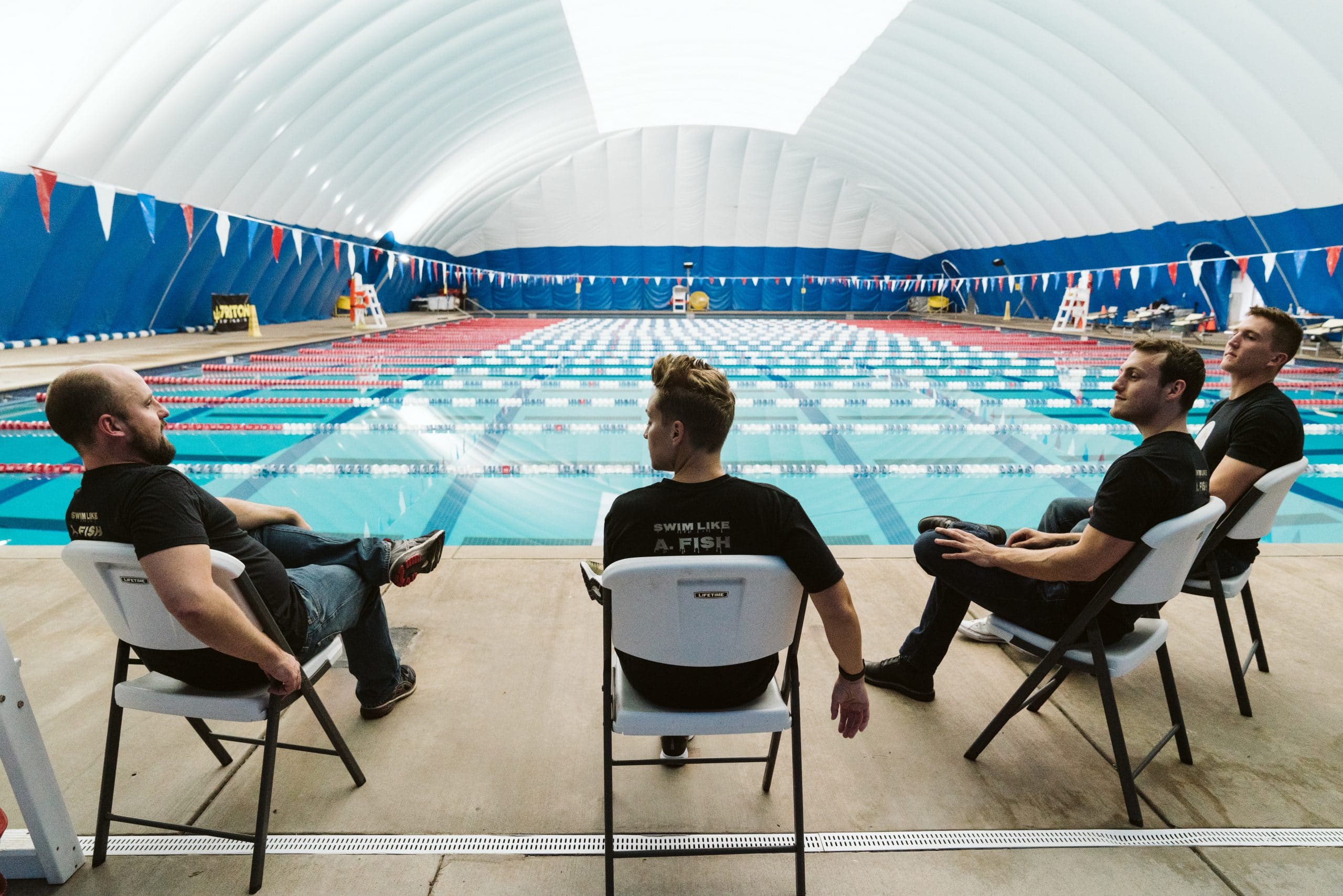 Swim Like A. Fish team sitting by an indoor swimming pool.