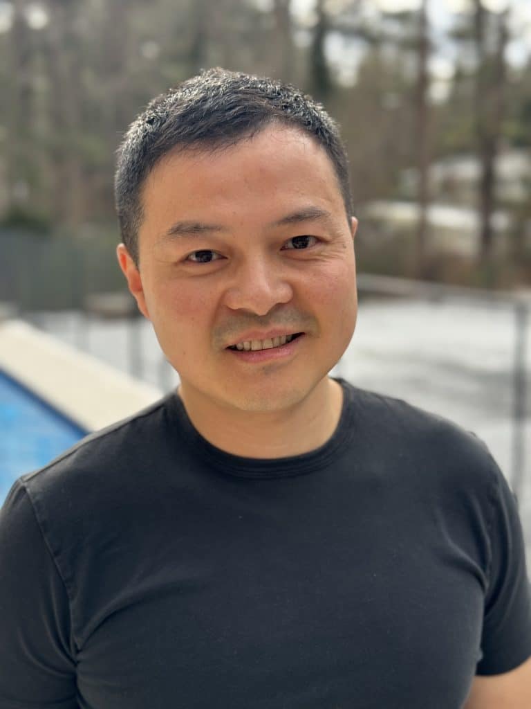 Scott Zhang wearing a black t-shirt standing by a swimming pool.