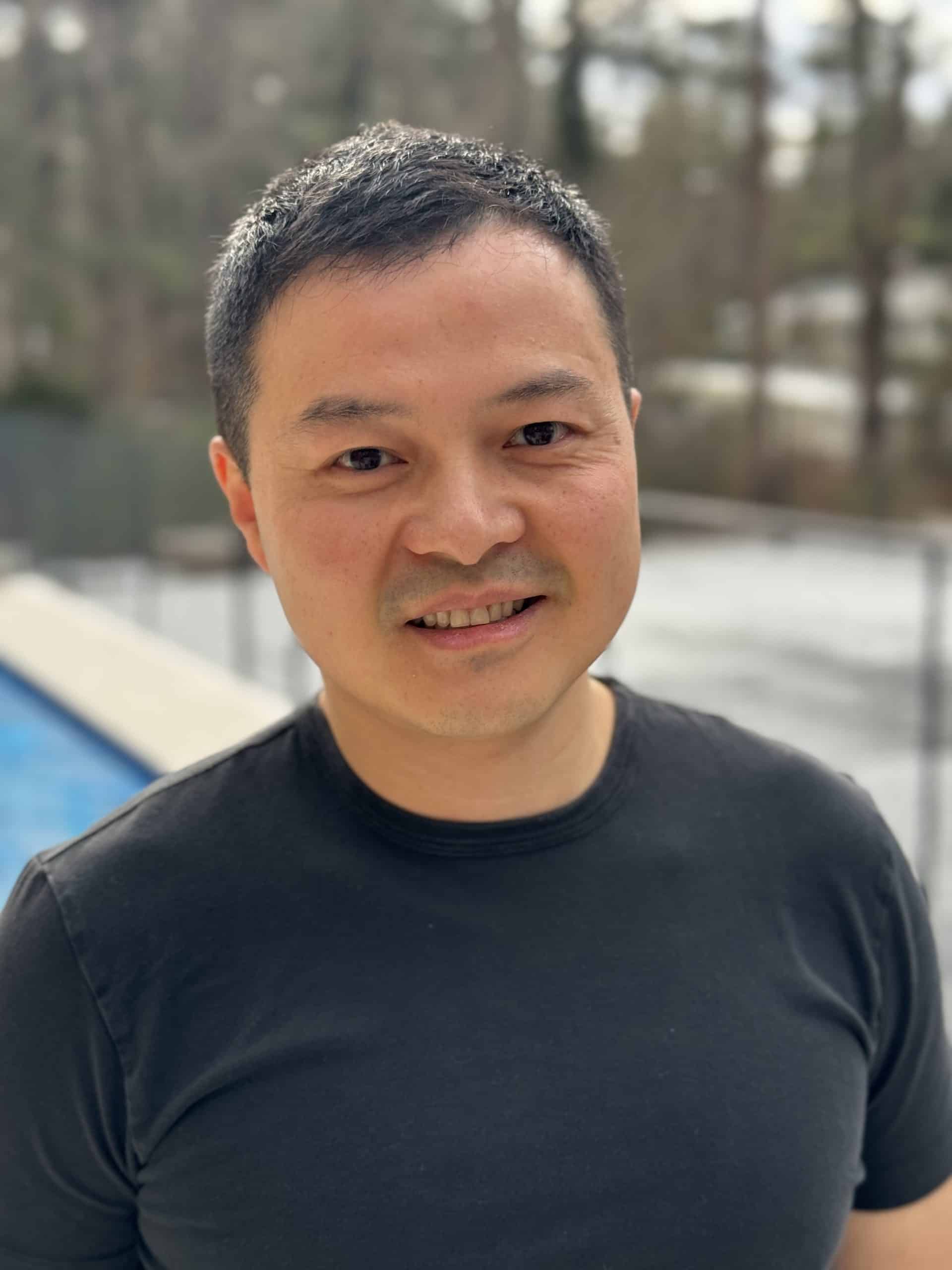 Scott Zhang wearing a black t-shirt standing by a swimming pool.